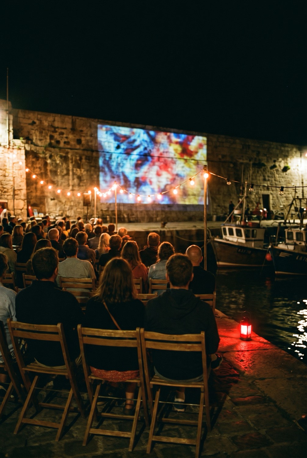 An open-air film projected on the old harbour wall, the audience on folding chairs