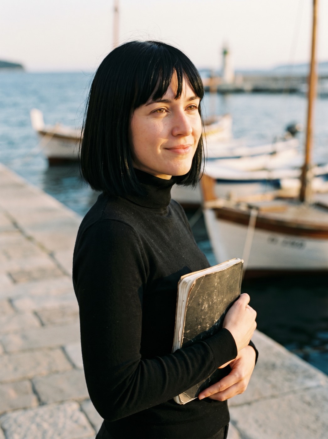 Sara Pertot, a writer in a black turtleneck, with a notebook under her arm